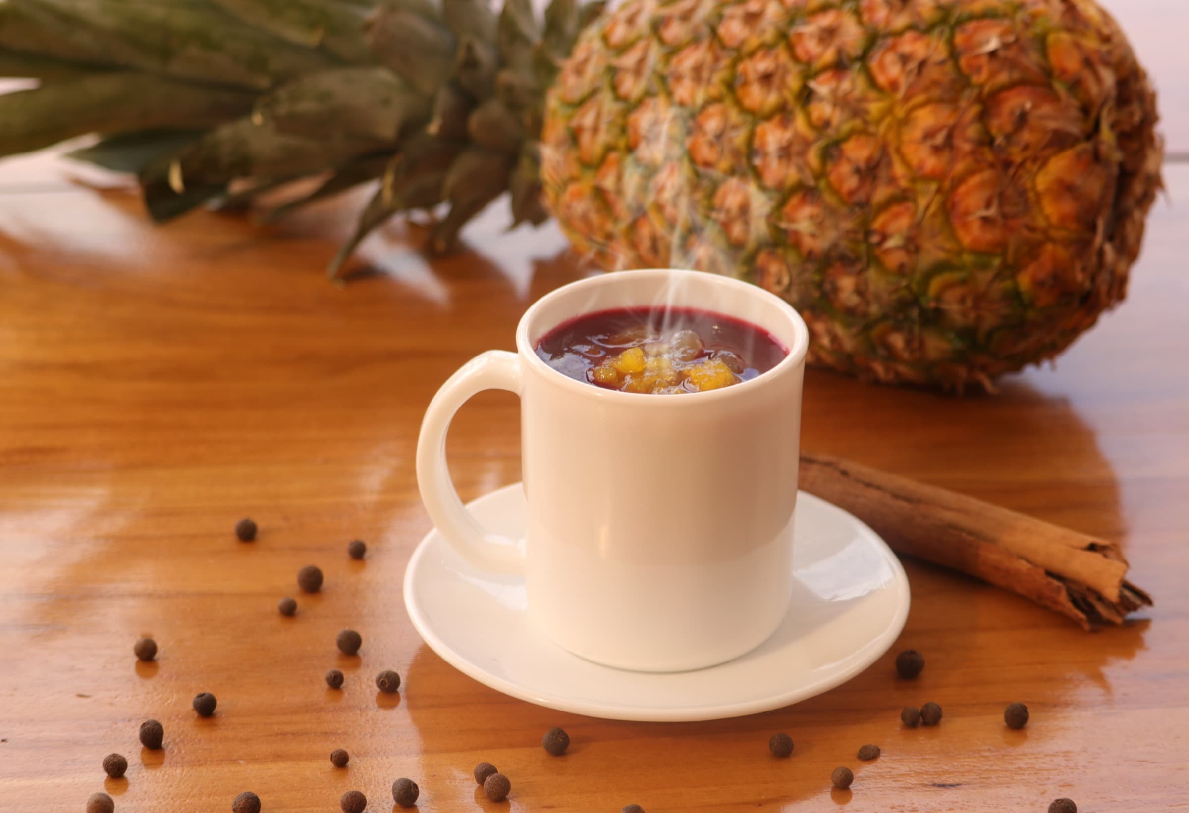 Taza de colada morada caliente de Morada Colada, servida con piña, canela y pimienta dulce sobre una mesa de madera en Quito